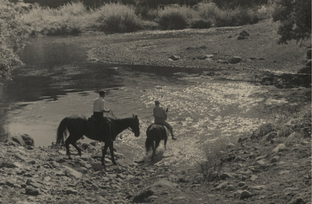Two men on horseback crossing ford.